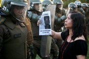 A woman shows a picture of Mapuche indigenous man Camilo Catrillanca, who was killed by security forces, to riot police during a protest in Santiago, Chile, Nov. 19, 2018 (AP photo by Esteban Felix).