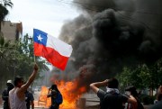 An anti-government protester waves a Chilean flag during clashes with police amid a general strike in Santiago, Chile, Oct. 23, 2019 (AP photo by Luis Hidalgo).