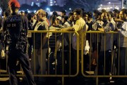 A police officer watches over migrant workers as they wait for shuttle buses to take them back to their dormitories, Singapore, Feb. 9, 2014 (AP photo by Joseph Nair).