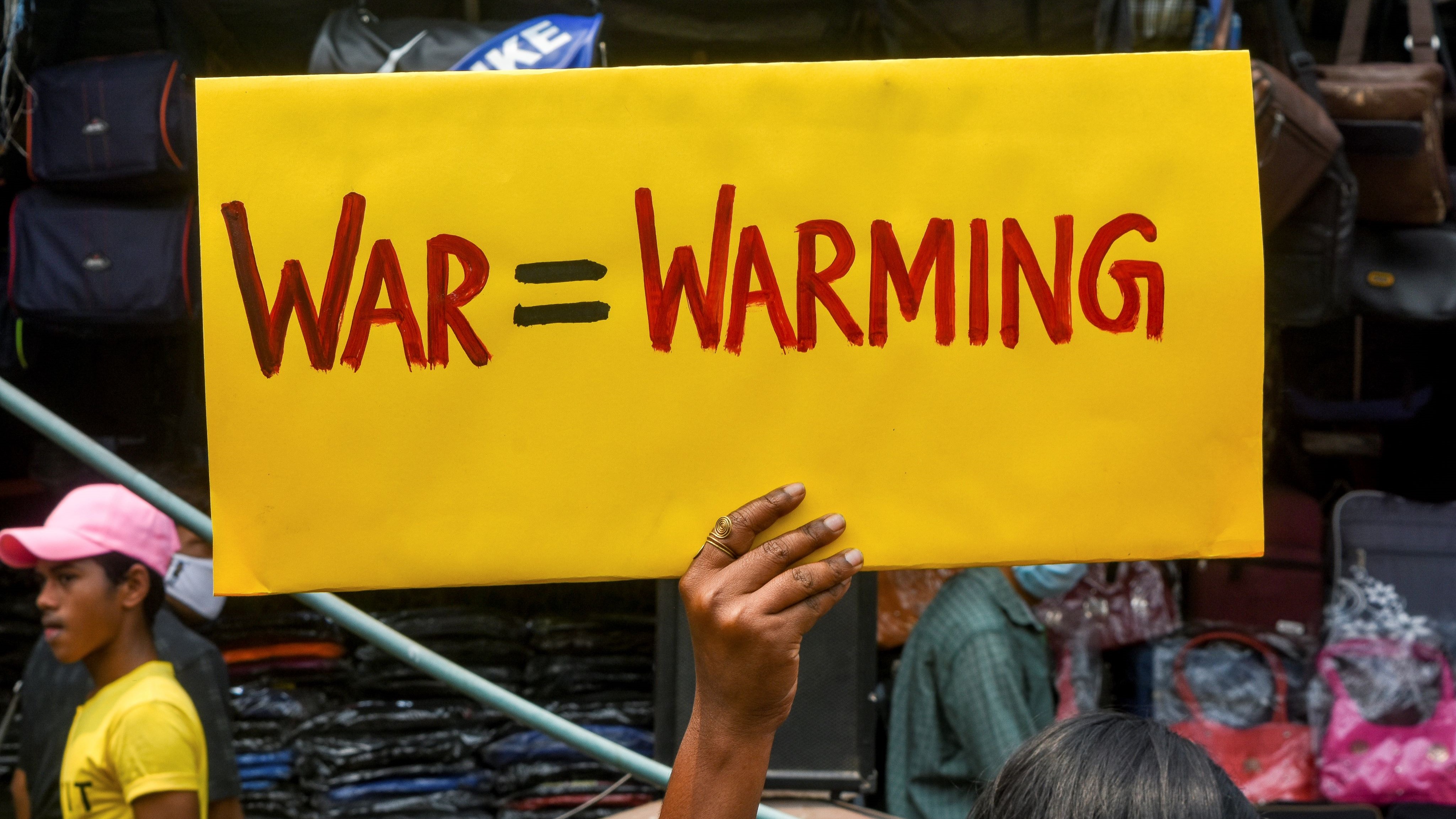 An activist holds a sign reading "war=warming."