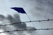 A European Union flag hangs from barbed wire.