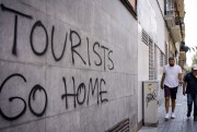 Two men walk past a graffiti reading “Tourists Go Home” in Barcelona.