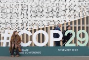 An attendee sits on a sign for the U.N. COP29 Climate Change Conference.