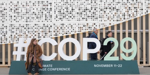 An attendee sits on a sign for the U.N. COP29 Climate Change Conference.